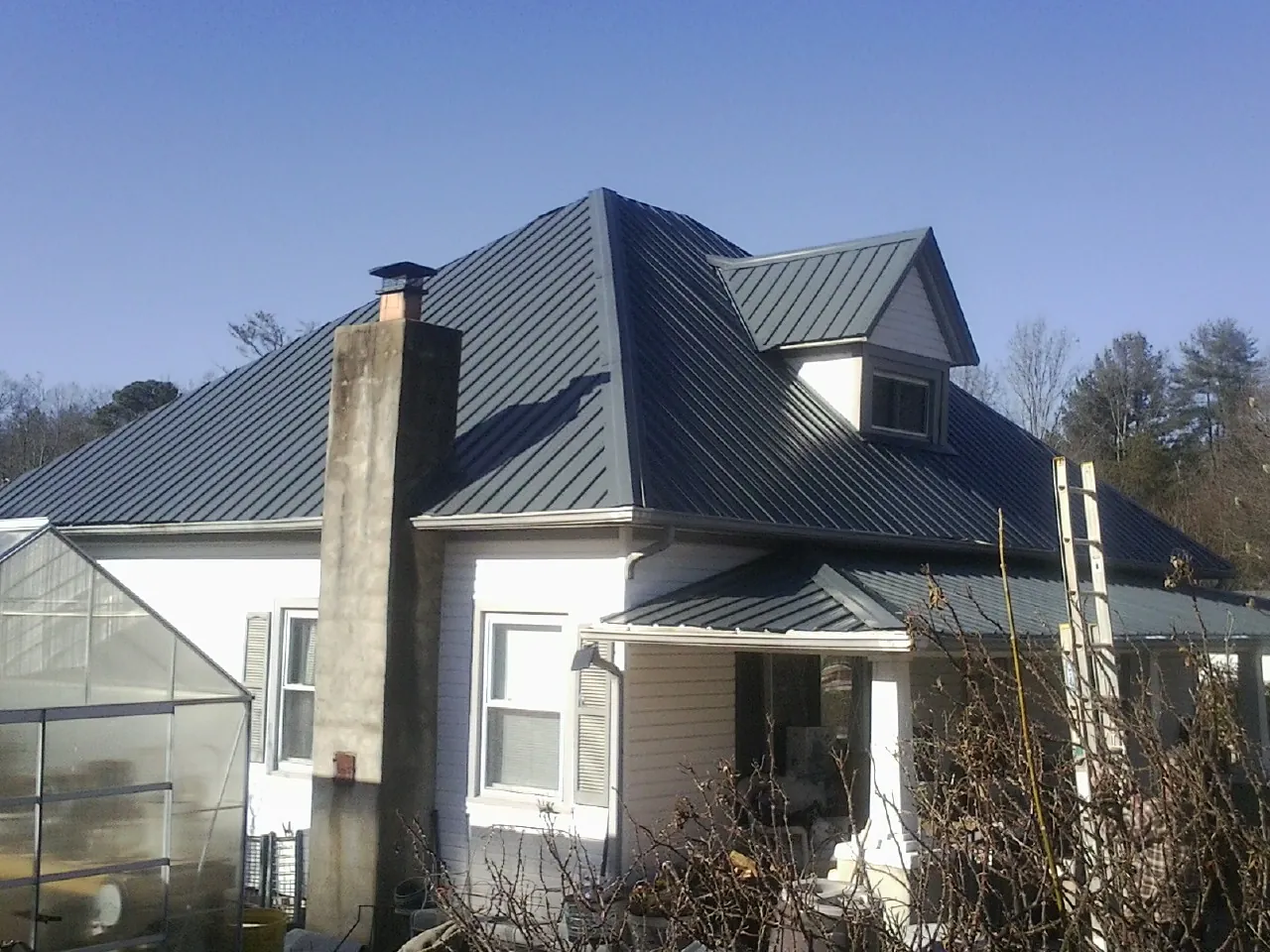 Dark blue standing seam metal roof on a white farmhouse with dormer — Slate & Tile Roof Repair by Roofing Brothers in Closter