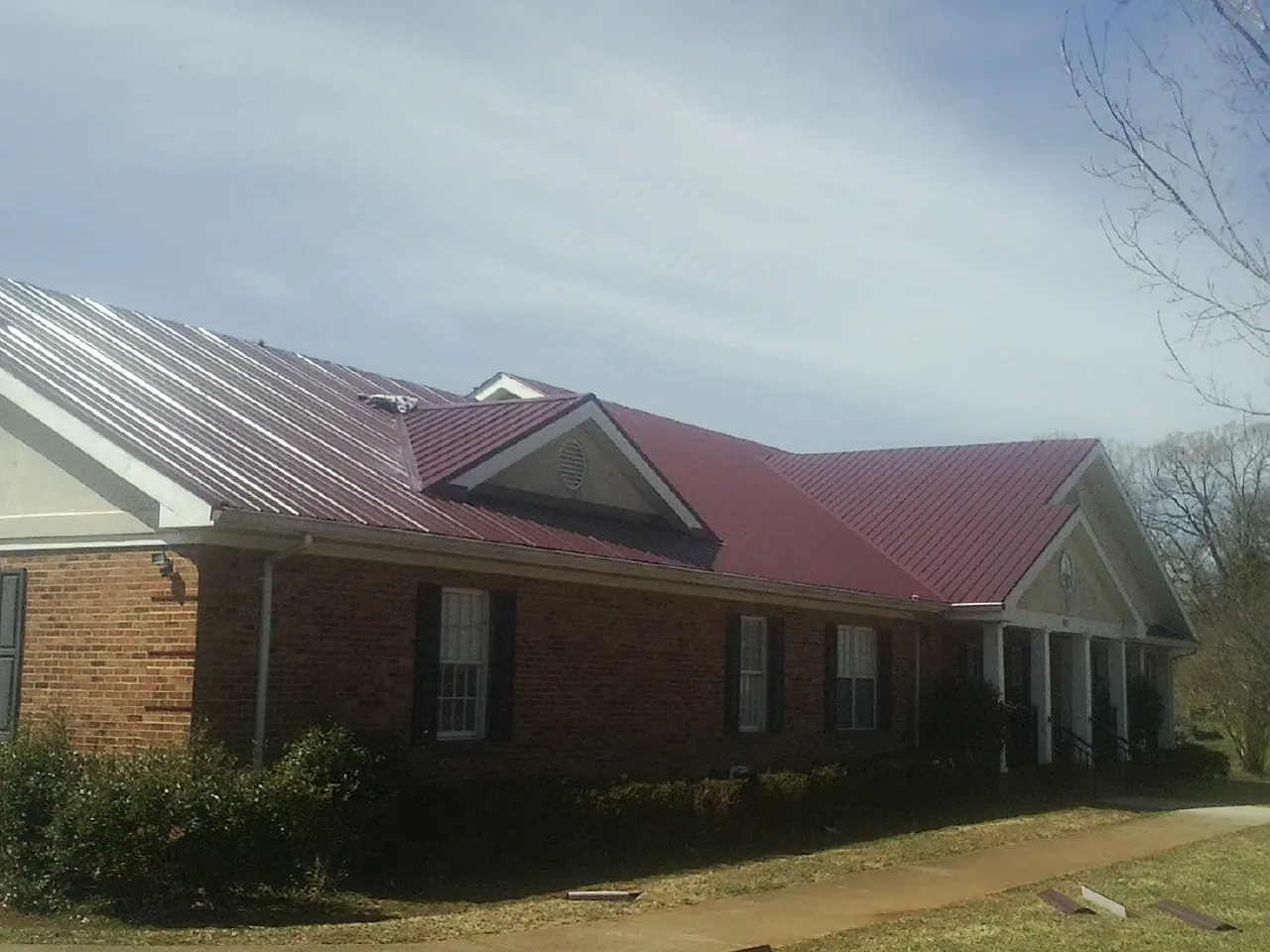 Red metal roof with gabled entries on a long brick building, from a Hail Damage Roof Repair job in Closter
