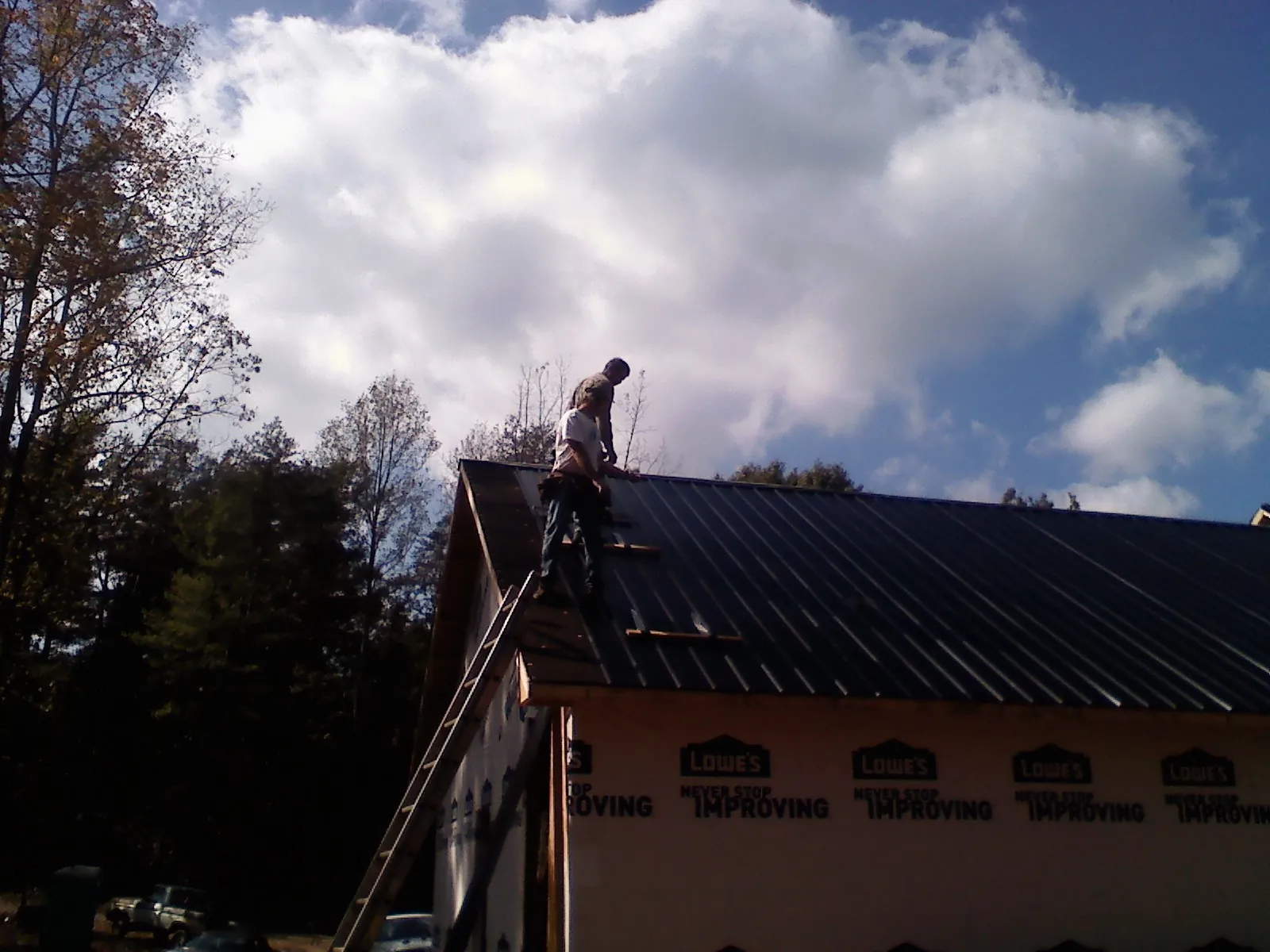 Roofer fastening dark metal panels high against a cloudy sky, from a Roof Inspection job in Closter
