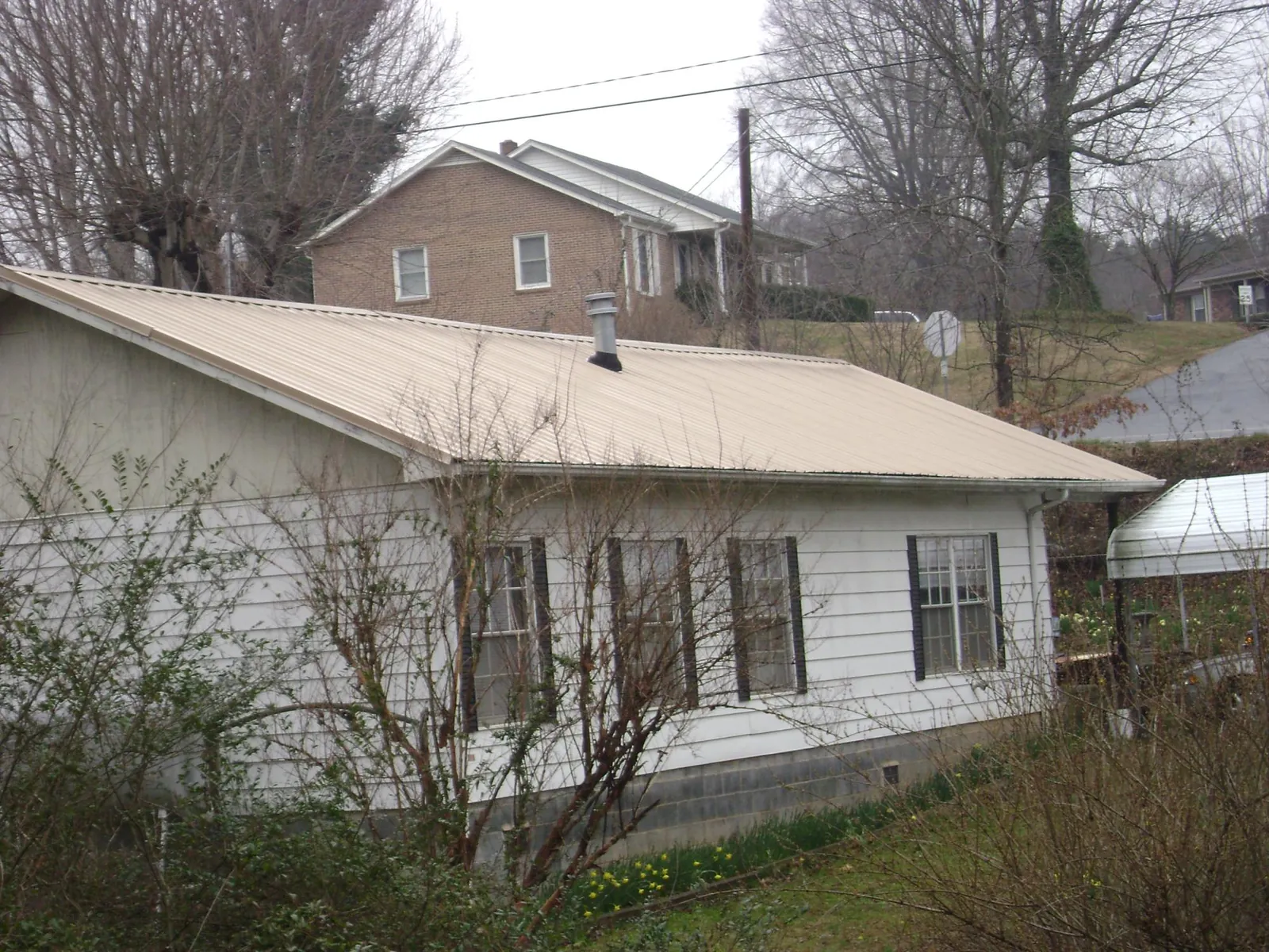 Tan metal roof on a white sided house set into a hillside — Commercial Roofing by Roofing Brothers in Closter